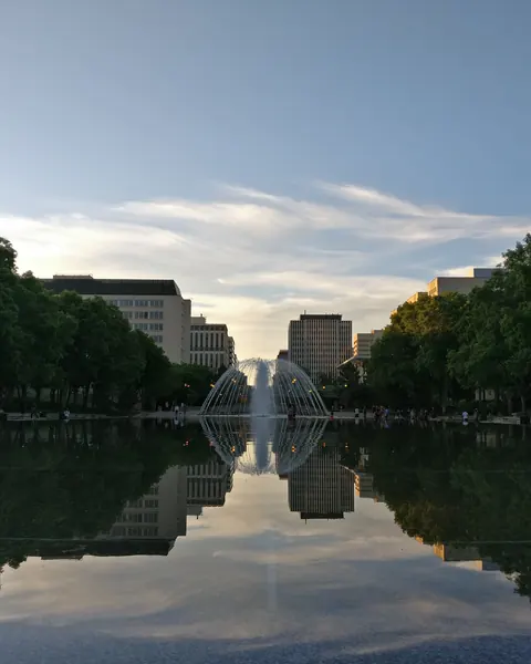 The Alberta Legislature reflecting pool and fountain in Edmonton at dusk, framed by trees and downtown towers