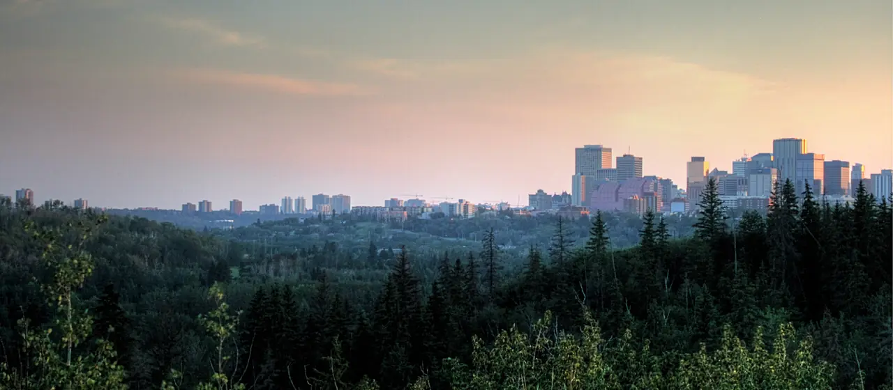 Forested North Saskatchewan River valley at dusk with the distant downtown Edmonton skyline, seen from Highlands